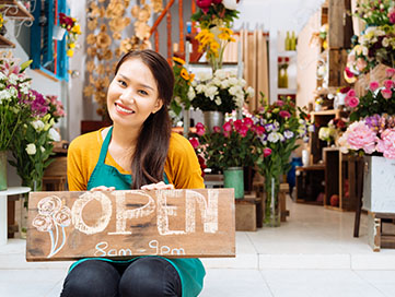 Owner of a floral shop holding open sign